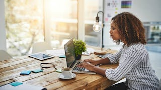 A brunette woman in a white-gray shirt typing on a white laptop who quit her job but not to spend mo...