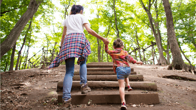 A woman and her stepdaughter going up wooden stairs in the forest.