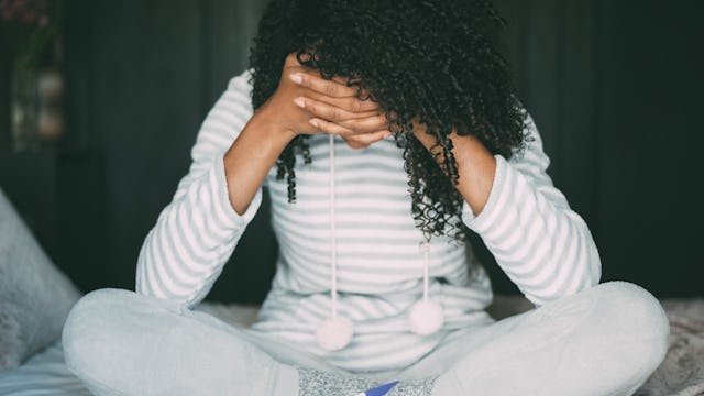 Desperate woman sitting on the bed wearing pajamas, holding her face with her hands