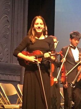 A girl wearing a black dress on a stage while holding a violin