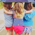 The back of three little girls walking under the umbrella while hugging