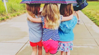 The back of three little girls walking under the umbrella while hugging