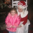 1 A woman dressed as Santa and sitting in a white wooden chair, holding closely a blonde toddler gir...