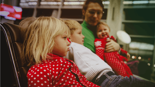 A parent holding one of his children and other two children sitting next to them at the airport