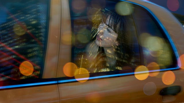 A woman sitting in the back of an Uber vehicle with city lights reflecting on the windows