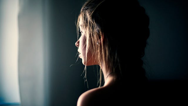 A tween girl standing in the dark while looking through a window.