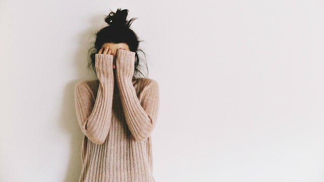 A teen with OCD standing and covering her face with her hands.