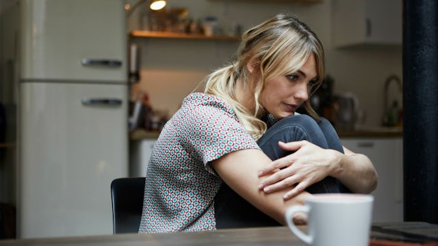 A mother sitting in the kitchen during the process of getting sober with a white mug on a wooden tab...