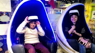 Two tweens having fun in a Virtual Reality Center sitting in two gaming pods