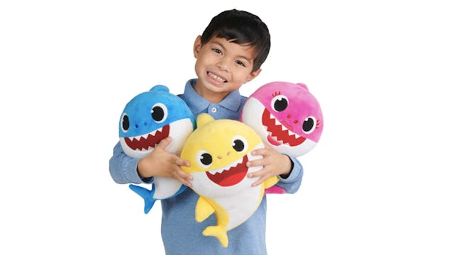 A boy holding singing "Baby Shark" plushes in blue, yellow and pink