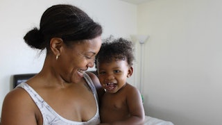 A dark-haired woman in a white tank top holding her son and both are smiling
