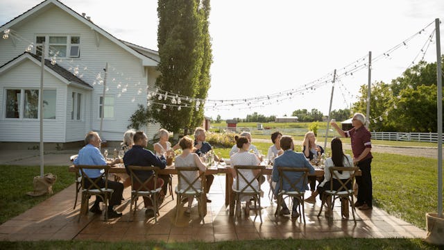A group of people sitting at the table on wooden chairs outside with in-laws giving a toast