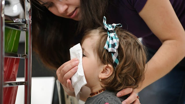 A mother in a black T-shirt wiping her sick daughter's nose 