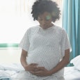 A pregnant woman is sitting on a hospital bed and holding her belly and she has a high risk pregnanc...