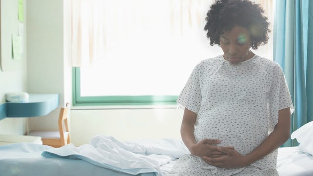 A pregnant woman with a high risk pregnancy sitting on a hospital bed and holding her belly