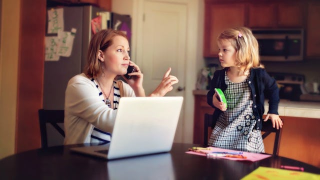 A woman sitting with a laptop in front of her and speaking on her phone while pointing a finger at h...