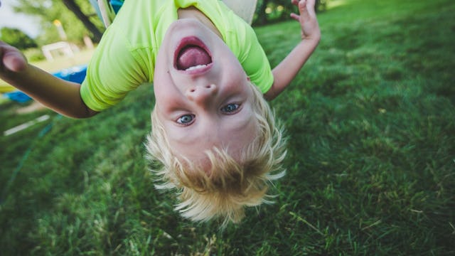 Upside down photograph of a young blonde boy screaming while playing on the grass