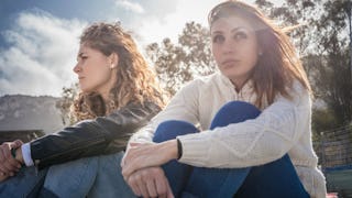 A woman in a brown top and denim jeans next to a woman in a white top and blue denim jeans who have ...