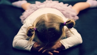 A blonde toddler girl wearing a white shirt and pink skirt lying on the floor while having a tantrum...