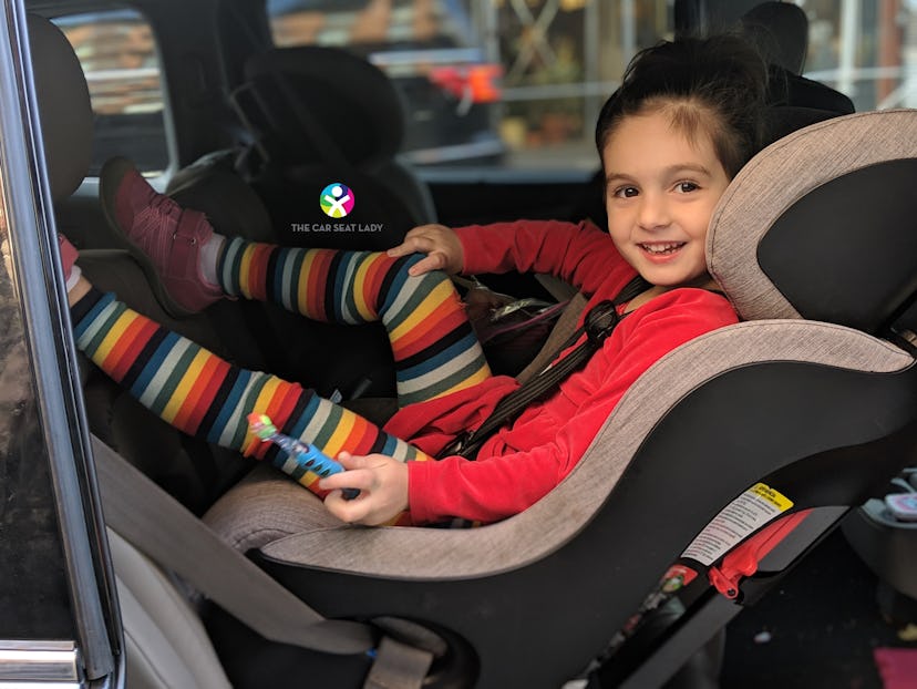  A little girl in red T-shirt and colorful leggings sitting in her car seat and smiling.