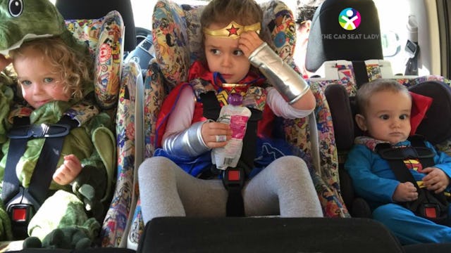 Three kids, two girls and a little boy sitting next to each other in their car seats.