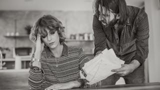 A woman in distress sitting on a chair and a man angrily showing her divorce papers