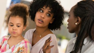 A mother and her daughter with curly hair talking to her teacher in school