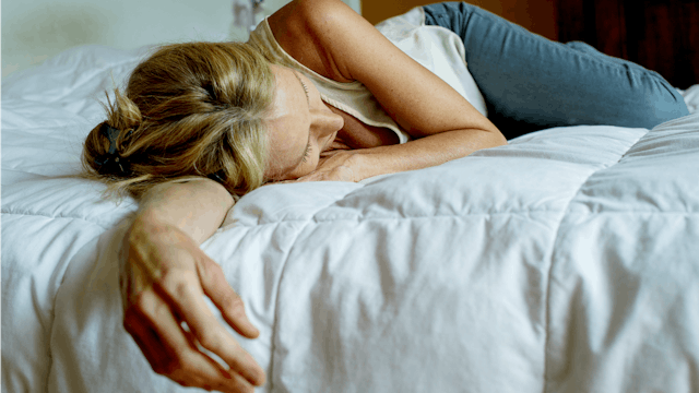 A woman in a white top and blue denim jeans lying on a bed leaning on one stretched out hand