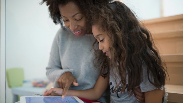 A mother sitting next to her daughter while showing her something on a tablet
