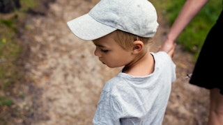 A neurodivergent boy in a grey shirt and a cap walking with his mother