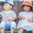 A boy in a blue-white striped T-shirt, blue denim jeans, and a cap blowing bubbles next to a girl in...