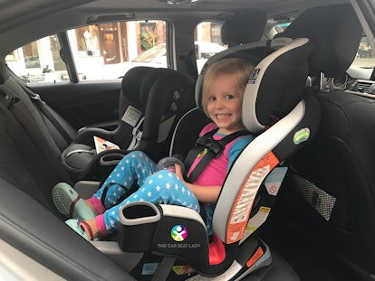 A little blonde girl sitting in her car seat smiling.