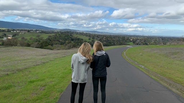 Two female friends standing alone on a road that is surrounded by a valley