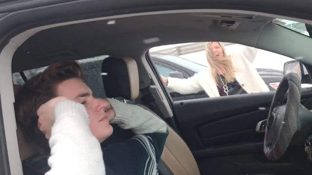 A teen sitting in a car, covering his ears, while his mum is outside, yelling and embarrassing him