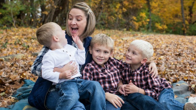 A mother playing in a pile of leaves with her three sons in an all boy family