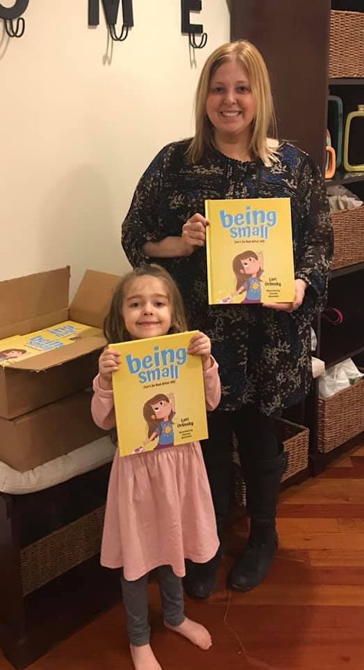 A mother and a daughter holding books for kids called "Being small"
