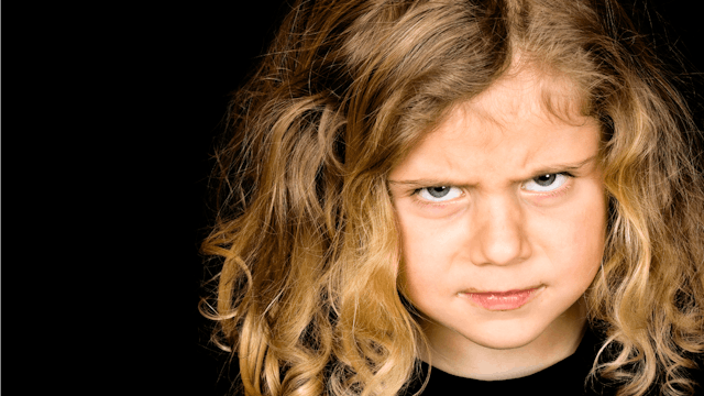 A tween girl with a mean face and curly brown hair