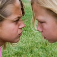 Two blonde girls wearing pink shirts looking at each other angrily, bullying each other