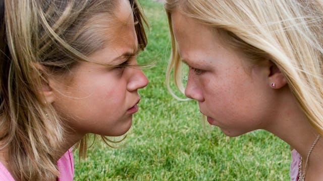 Two blonde girls wearing pink shirts looking at each other angrily, bullying each other
