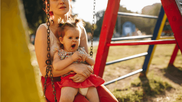 A mother holding her baby daughter on her lap while sitting on a swing