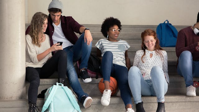 Four teen kids during non-class activities in high school sitting on steps in a school hall
