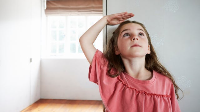 A small girl checking her height on a wall