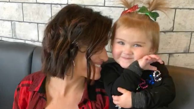 Heather Shurina, with brown hair, is smiling while her child sitting next to her on the couch