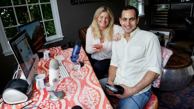 Happily married couple posing together in front of their computer, where they film their podcast.