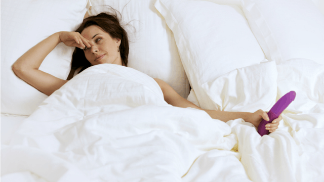 Woman in her 40s laying in the bed with a vibrator in her hand