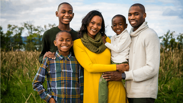 Young black parents happily posing outdoors with their three sons, each of different ages.