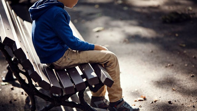 A young boy ghosted by his father sitting alone on a bench