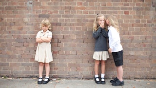 Two girls acting like mean girls, gossiping about a girl standing next to them.