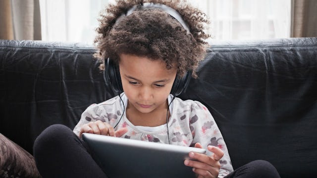 A kid with his earphones on watching YouTube videos on an iPad