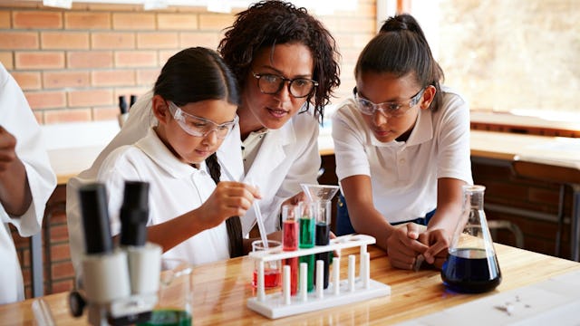 A teacher and two students wearing lab coats in science class